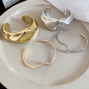 Irregular crumpled gold and silver open cuff bracelets on a white ceramic plate.