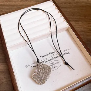 Detailed view of a silver textured pendant on an adjustable black leather cord necklace