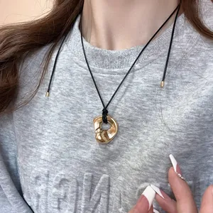 Close-up of a gold geometric pendant on a black cord necklace worn on a gray sweatshirt