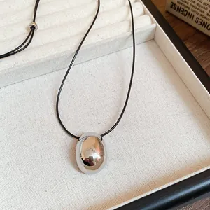 Close-up of a minimalist silver oval pendant on a black cord necklace in a display tray.
