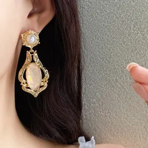 Close-up detail of vintage gold earrings with an oval shell stone worn on an Asian model