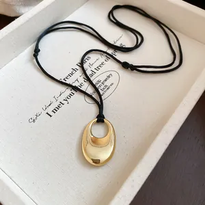 Detailed view of a polished gold oval pendant on a minimalist black adjustable cord necklace