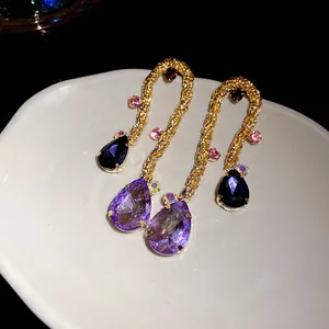 Detailed close-up of vintage woven gold earrings featuring large purple and blue water drop crystals