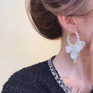 Dettaglio ravvicinato di orecchini a cerchio con perle e pendenti a petalo bianco eleganti