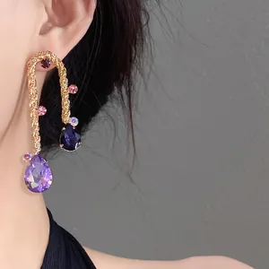 Close-up of vintage-style gold twisted drop earrings featuring teardrop purple crystals.