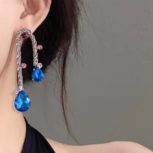 Detailed view of silver braided earrings with blue teardrop crystals worn by model