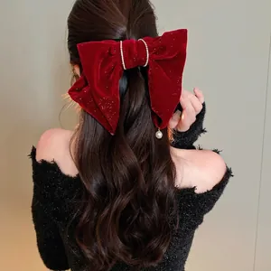 Gros plan sur une grande pince à cheveux en velours rouge ornée de strass et d'une perle