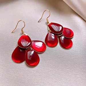 Close-up of elegant red enamel teardrop earrings with vintage gold-plated hooks.