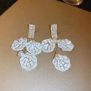 Vista dei dettagli di eleganti orecchini a fiore con perle e texture craquelé dorata bianca.