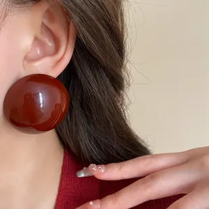 Close-up view of vintage dark red oversized round dome stud earrings worn by a model