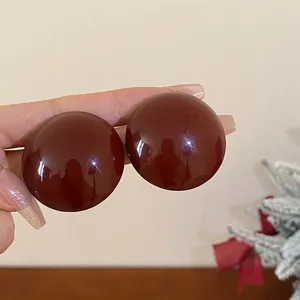 Close-up macro view of oversized glossy burgundy round stud earrings with a smooth finish