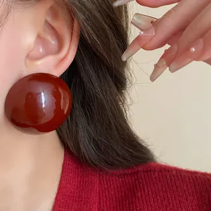 Detail view of vintage style oversized burgundy glossy round stud earrings worn on ear