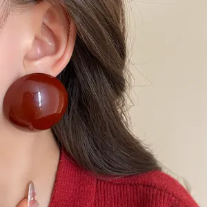 Detail view of large dark red glossy round stud earring worn on model ear.