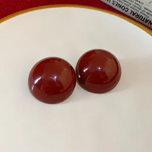 Close-up detail of glossy dark red round dome stud earrings with retro geometric design