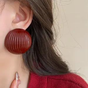 Macro view of oversized burgundy ribbed round earrings with a vintage glossy finish