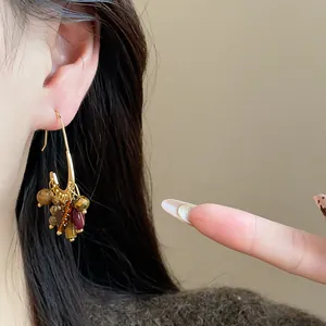 Close-up of retro ethnic gold-plated earrings with colorful stone tassels on ear.