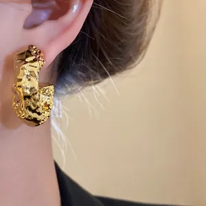 Close-up of vintage irregular hammered gold hoop stud earring with metallic texture.