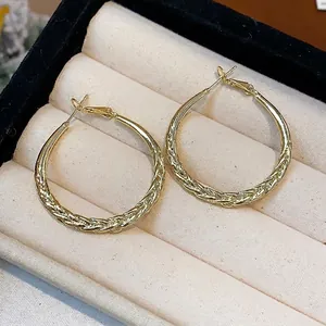 Elegant gold-tone twisted hoop earrings with a textured braid design in a jewelry box