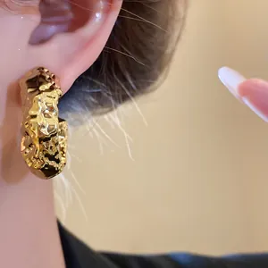 Detailed close-up view of a gold irregular wrinkled hoop earring worn on the ear lobe