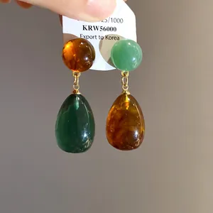 Detailed view of asymmetric resin waterdrop earrings with vintage amber and green beads
