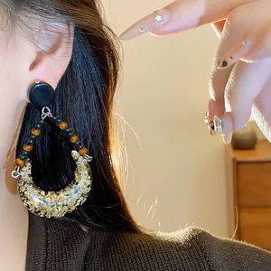 Close-up of vintage teardrop earring with gold foil resin and elegant beaded details on ear