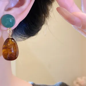 Close-up of vintage resin teardrop earrings with green stud and amber pendant detail.