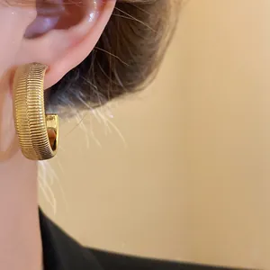 Close-up of gold-plated irregular pleated hoop earrings on a model's ear.