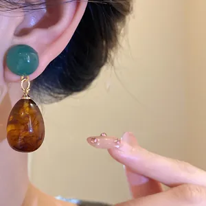 Close-up of vintage resin water drop earrings with amber and green stones in detail.