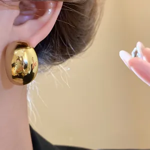 Close-up of large irregular gold dome earring with high-gloss metallic finish.