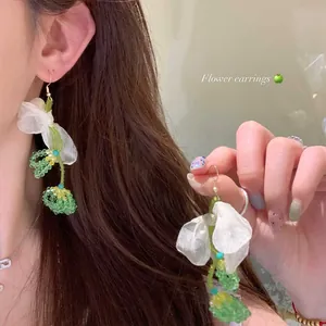 Detailed view of sweet white chiffon flower earrings with green beaded tassels on model