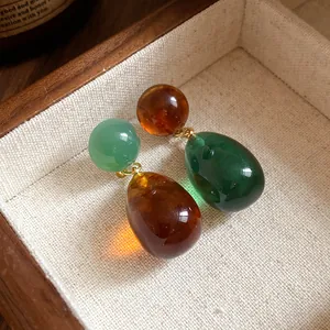 Close-up of asymmetric resin drop earrings in green and amber tones inside a wooden box