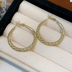 Macro shot of gold-toned hoop earrings with a detailed twisted braid texture in a box