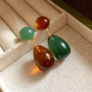 Close-up of vintage resin asymmetrical drop earrings in amber and green tones.