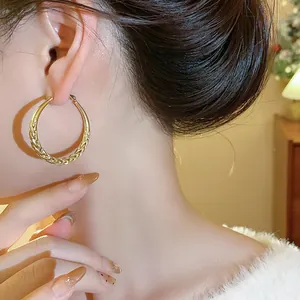 Detailed macro shot of gold-plated twisted pattern hoop earrings worn by a model