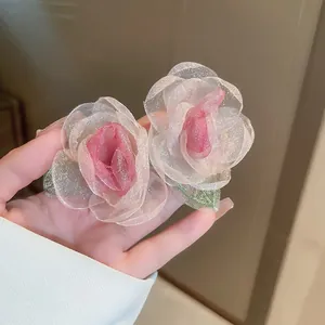 Macro shot of delicate pink chiffon rose earrings showing shimmering fabric detail.
