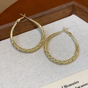 Detailed view of gold twisted hoop earrings on a textured fabric background