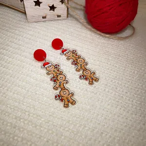 Close-up of festive stacked gingerbread man acrylic earrings with red studs