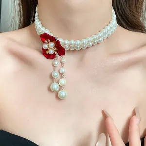 Detailed view of a retro palace style pearl choker with a red flower and pearl tassels.