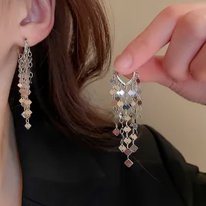 Close-up detail van zilveren lange kwastjes oorbellen met vierkante metalen plaatjes