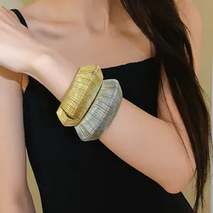 Close-up of layered gold and silver woven metal cuff bracelets on a model wrist