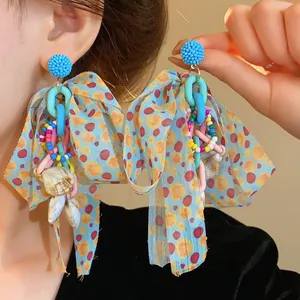 Macro detail of oversized bohemian bow earrings with colorful beads and natural shells