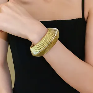Detailed view of a chunky gold metallic woven open bangle bracelet worn on wrist