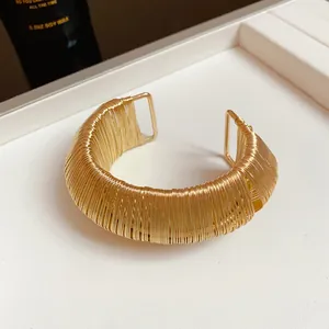 Macro view of a gold metallic woven open cuff bracelet showing fine wire texture.