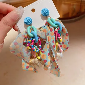 Close-up detail of colorful beaded bow earrings featuring shells and acrylic chains.