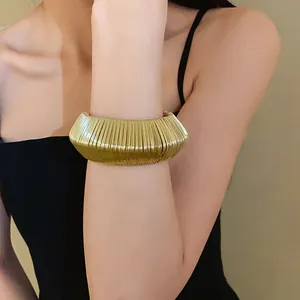 Detailed view of a wide gold-colored woven metal cuff bracelet on a model's wrist