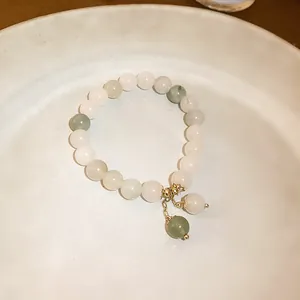 Detail view of an elegant jade bead bracelet with golden charms in a white ceramic dish