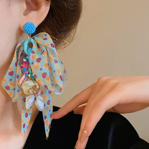Detail view of oversized blue ribbon bow earrings with colorful beads and sea shell charms.