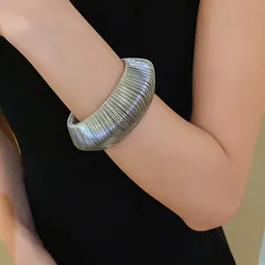 Detailed view of silver metallic woven wide cuff bracelet worn on a woman's wrist
