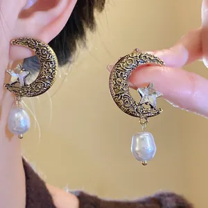 Detailed macro view of vintage moon and star earrings with a dangling baroque pearl drop