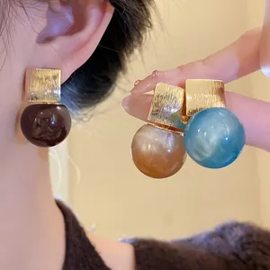 Close-up of candy-colored resin earrings with square gold-tone metal studs.